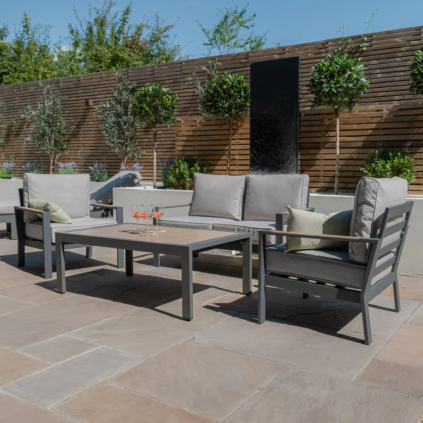 Grey outdoor garden sofa set with armchairs and rectangular coffee table on stone patio