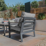 Grey garden armchair with metal frame and cushions on a stone patio, surrounded by greenery