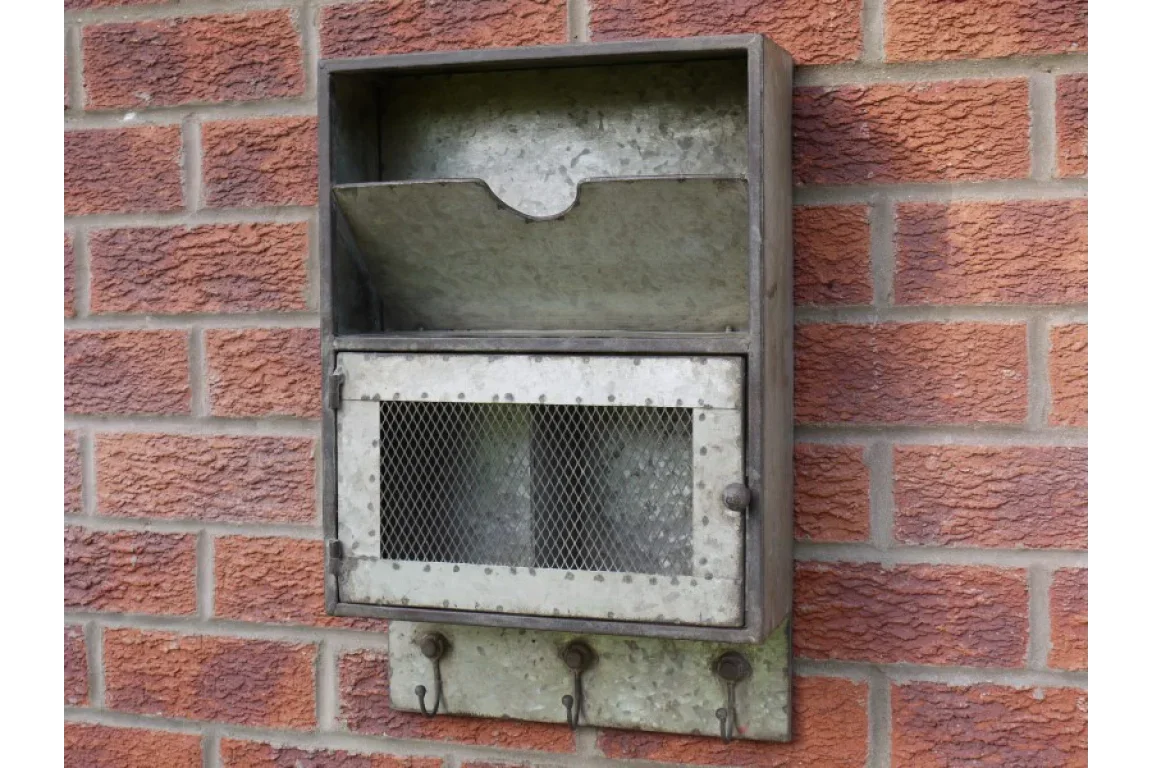 Galvanized metal wall organizer with mesh door and hooks mounted on brick wall