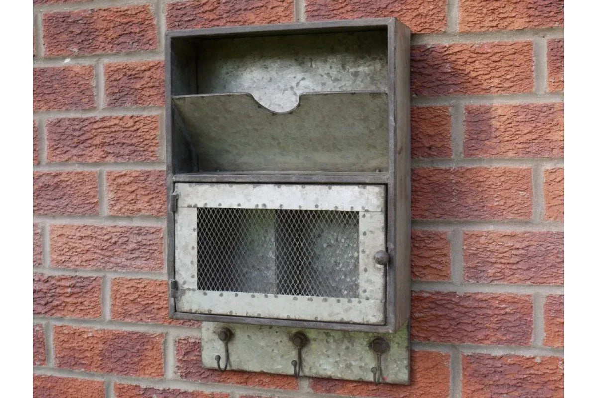 Galvanised metal wall-mounted letterbox with mesh door and key hooks on brick wall