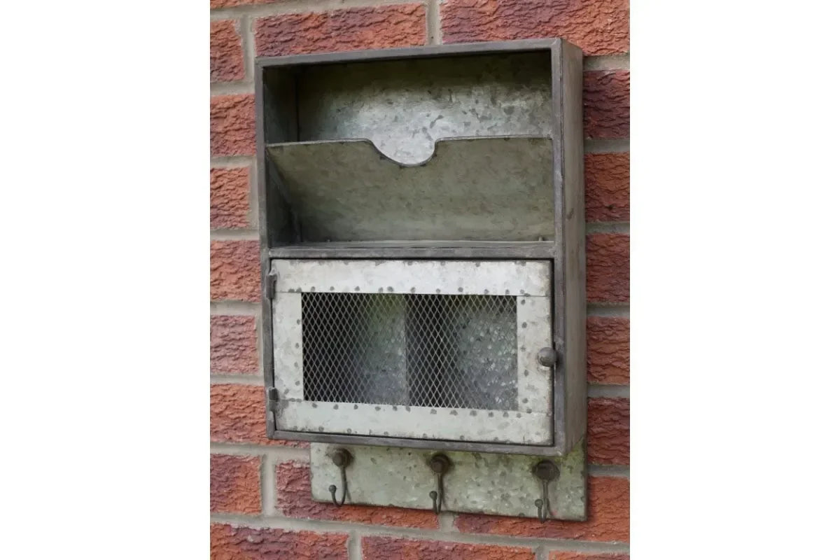 Galvanized metal wall organizer with mesh door and hooks mounted on brick wall