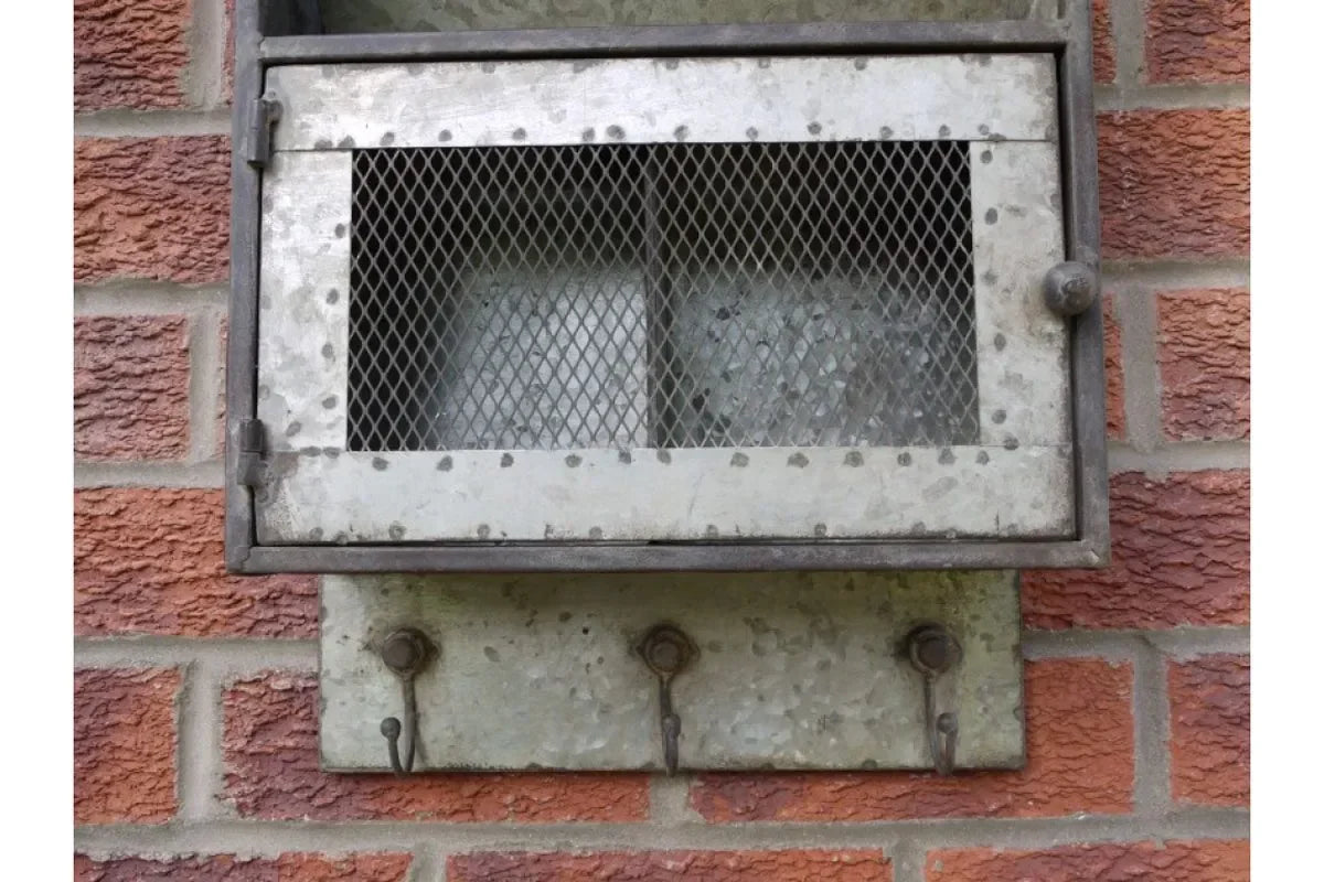 Galvanised metal milk delivery box with mesh front fixed to brick wall