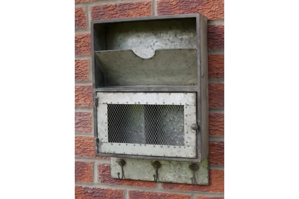 Galvanized metal wall storage box with mesh door and three hooks mounted on brick wall