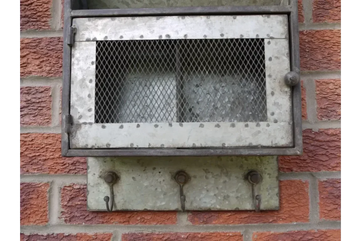 Galvanised metal outdoor key safe box with mesh front and hooks, mounted on brick wall