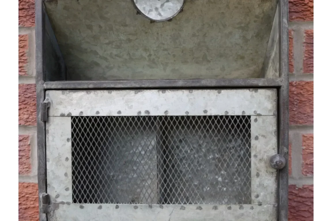Galvanised metal coal bunker with mesh door set against red brick wall