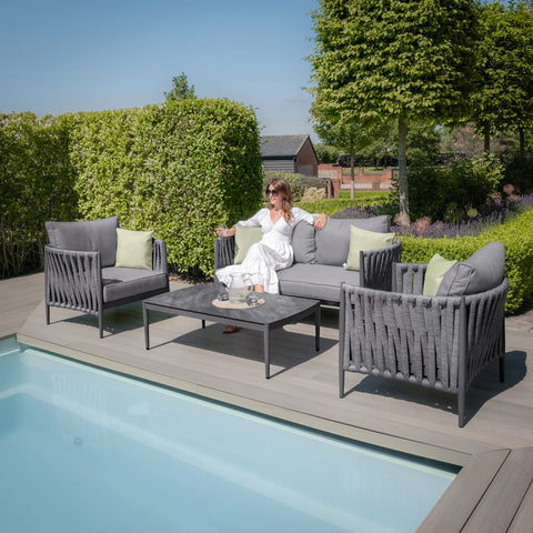 Grey outdoor sofa set with rope detailing beside a pool, woman seated on cushioned seat