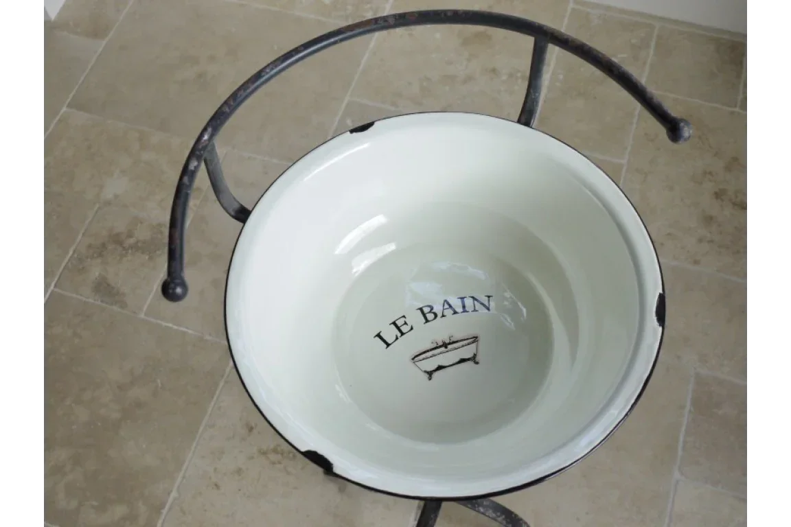 White enamel wash basin with 'LE BAIN' text on metal stand, placed on beige tiled floor