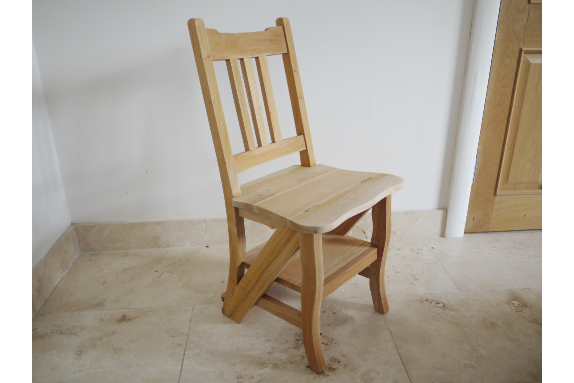 Unfinished natural wood chair with slatted backrest and built-in step viewed at an angle on tiled floor.