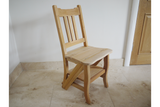 Unfinished natural wood chair with slatted backrest and built-in step viewed at an angle on tiled floor.