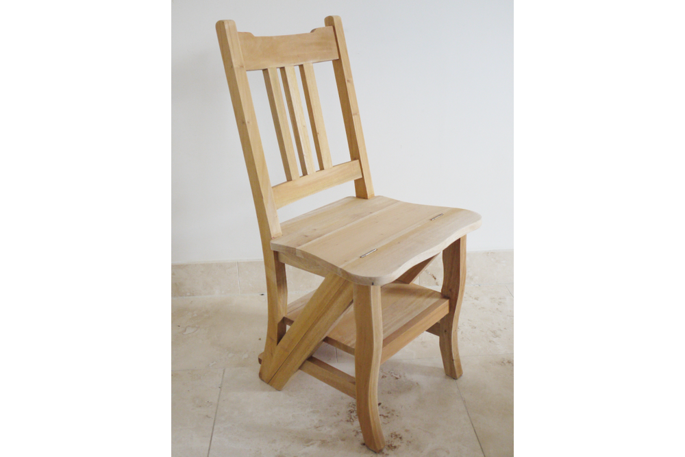 Unfinished light wood chair with vertical slat back, curved seat, and lower step shelf, shown from a side angle.
