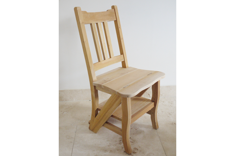 Unfinished light wood chair with vertical slat back, curved seat, and lower step shelf, shown from a side angle.