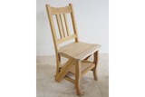 Unfinished light wood chair with vertical slat back, curved seat, and lower step shelf, shown from a side angle.