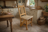 Unfinished light wood chair with step feature, straight backrest, photographed in a rustic kitchen setting from a side angle.