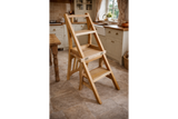 Unfinished wooden chair with built-in step ladder in a cozy kitchen setting, angled view showing steps and seat.
