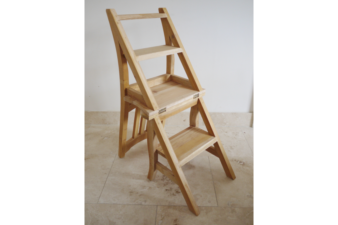 Unfinished light wood folding chair with built-in step ladder, angled view on beige tile floor against white wall