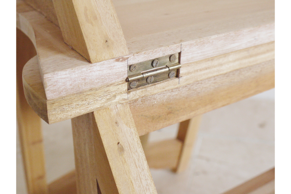Close-up of unfinished light wood chair step detail showing metal hinge and natural wood grain angle view.