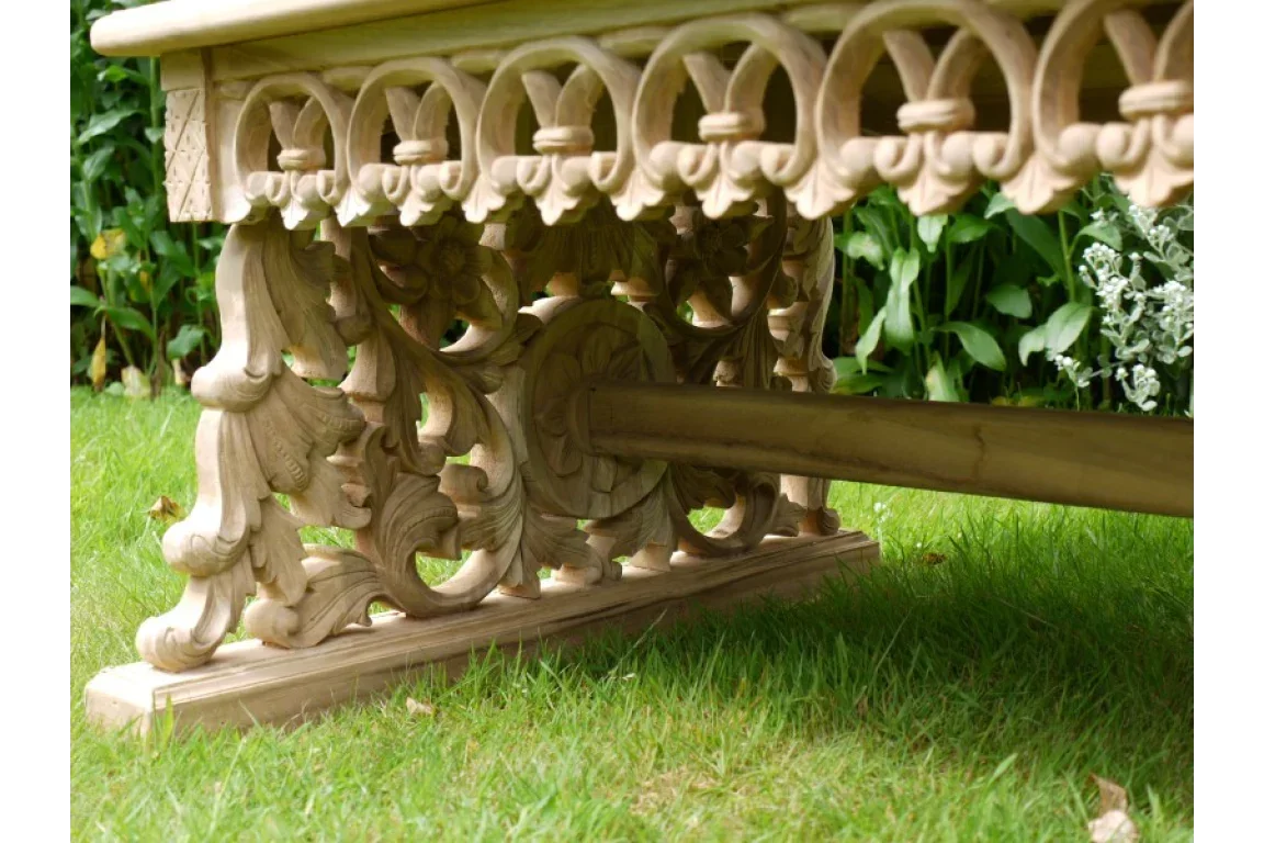 Carved wooden dining table base with ornate detailing on grass lawn