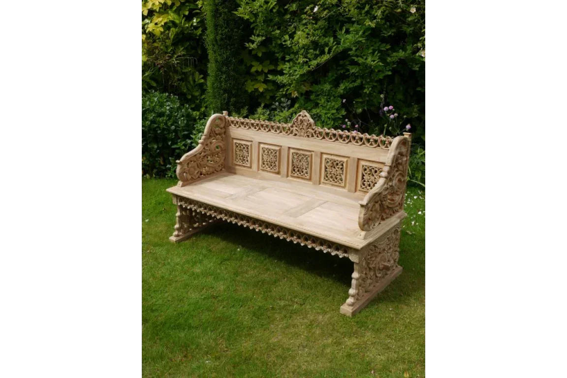 Hand-carved wooden garden bench with ornate backrest and armrests on lawn