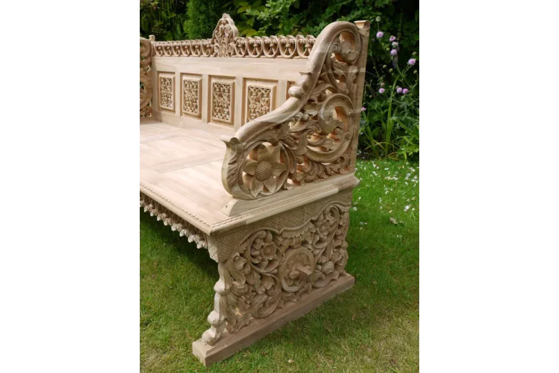 Teak wood carved garden bench with floral patterns on grass lawn