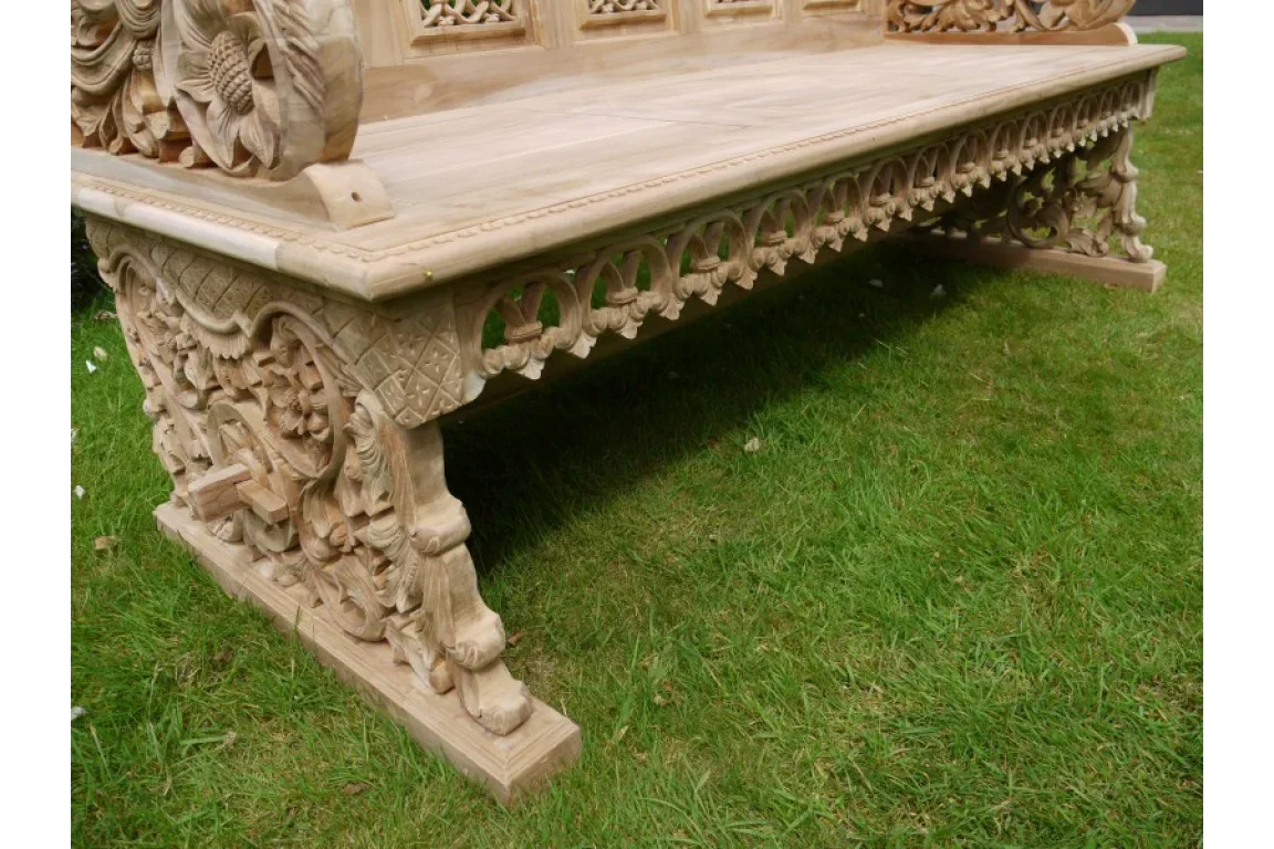 Carved wooden garden bench with floral patterns on legs and armrest on grass