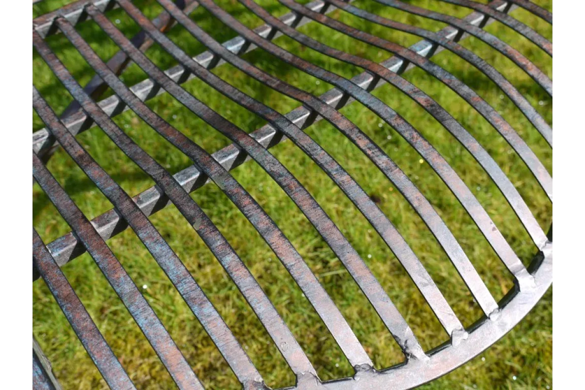 Closeup of curved metal garden bench seat with rust finish on grass
