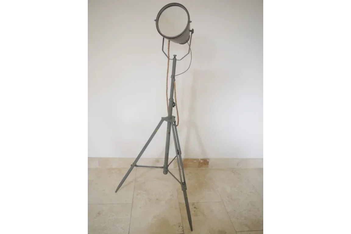 Industrial tripod floor lamp with metal frame and round shade against white wall
