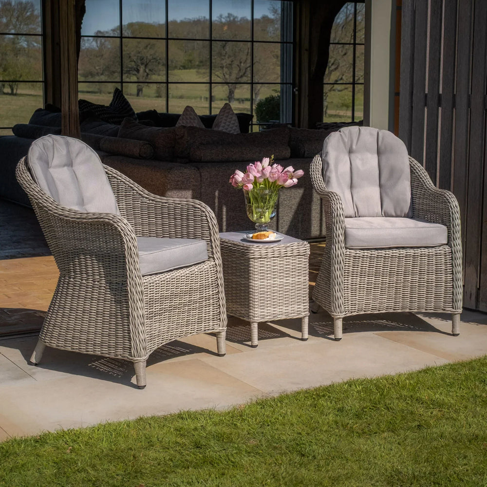 Grey rattan garden chair set with cushions and side table on patio, tulip vase on table