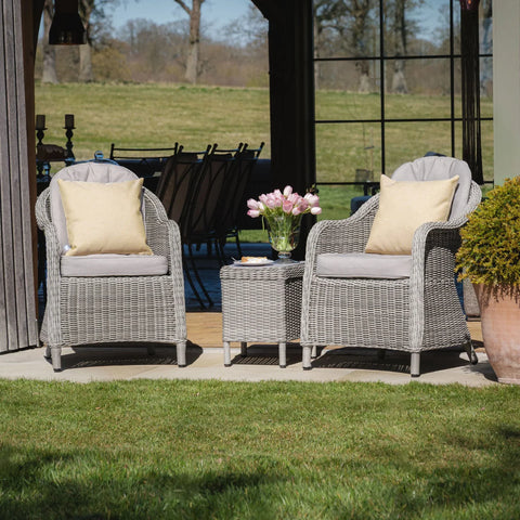 Grey rattan garden chairs with cushions and matching side table on patio