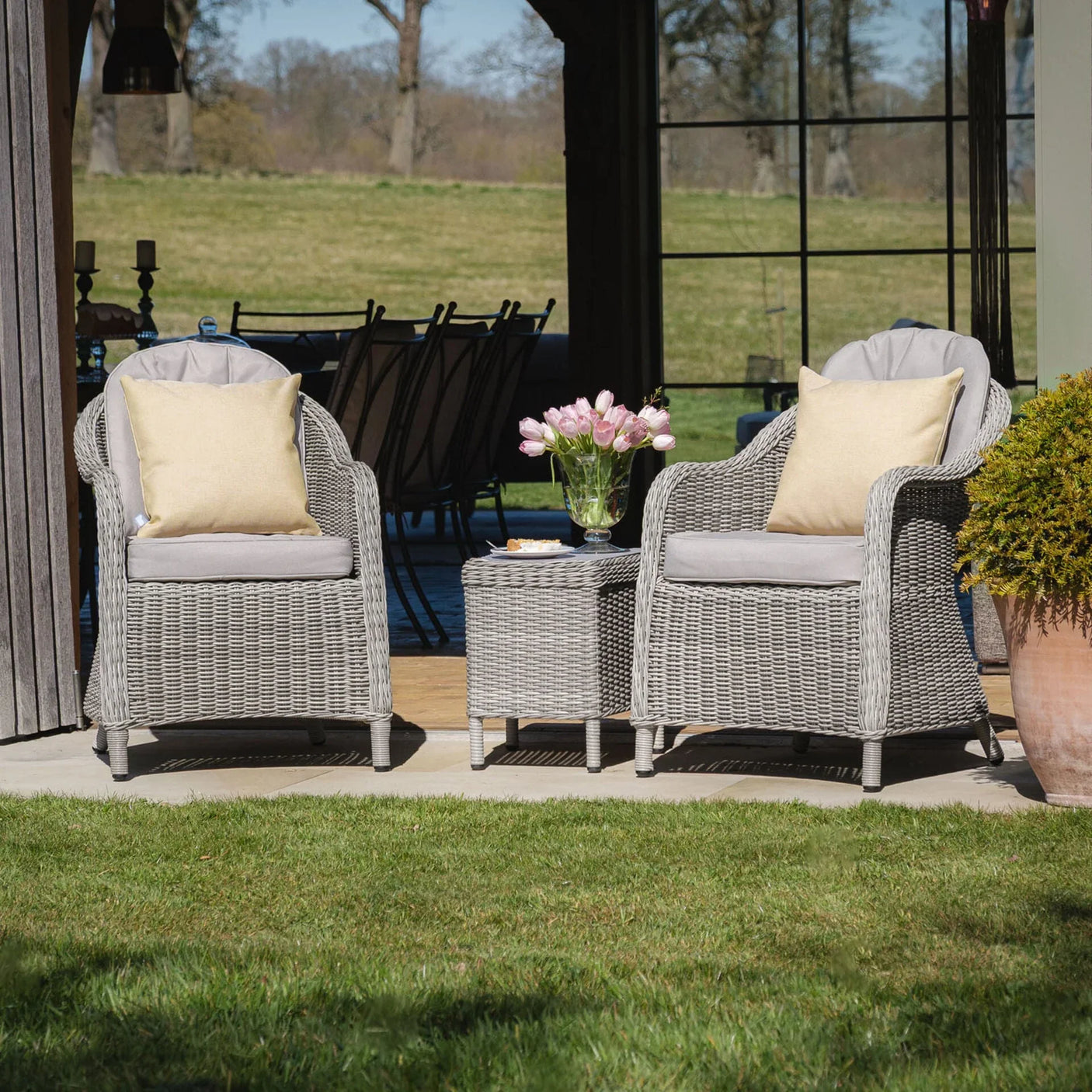Grey rattan garden chairs with cushions and matching side table on patio