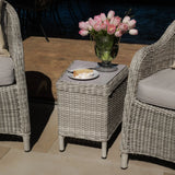 Grey rattan garden side table with glass vase of pink tulips and slice of cake on plate