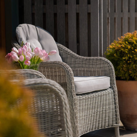 Grey rattan garden armchair with seat cushion on patio, tulips and potted plant nearby