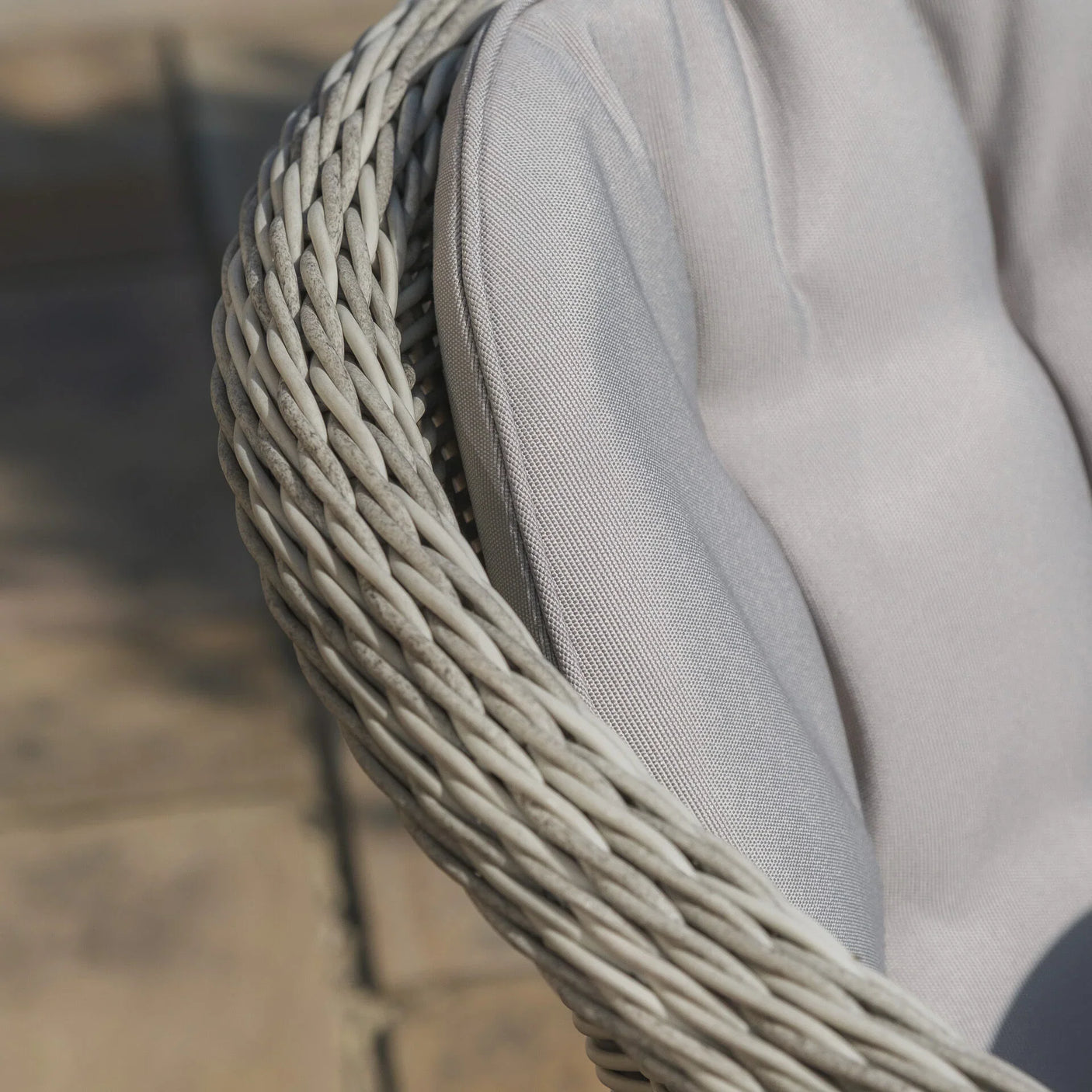 Closeup of rattan chair armrest with grey cushioned seat on outdoor patio
