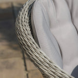 Closeup of rattan chair armrest with grey cushioned seat on outdoor patio