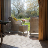 Rattan garden furniture set with two armchairs and table on patio, vase of pink flowers