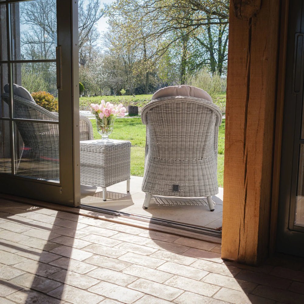 Grey rattan garden armchairs and side table on patio with flowers, view to lawn