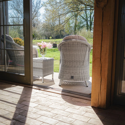 Grey rattan garden armchairs and side table on patio with flowers, view to lawn