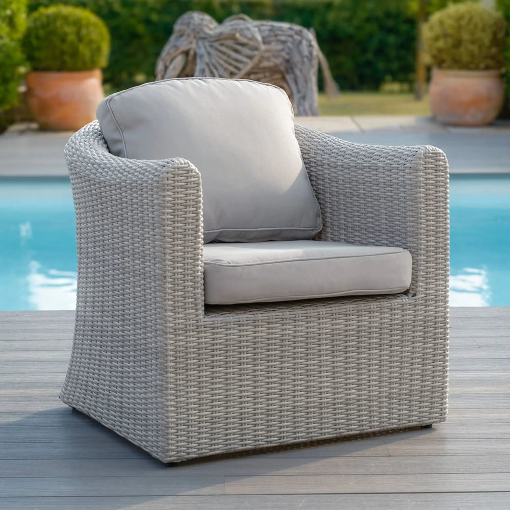 Light grey rattan outdoor armchair with cushions beside pool on wood decking