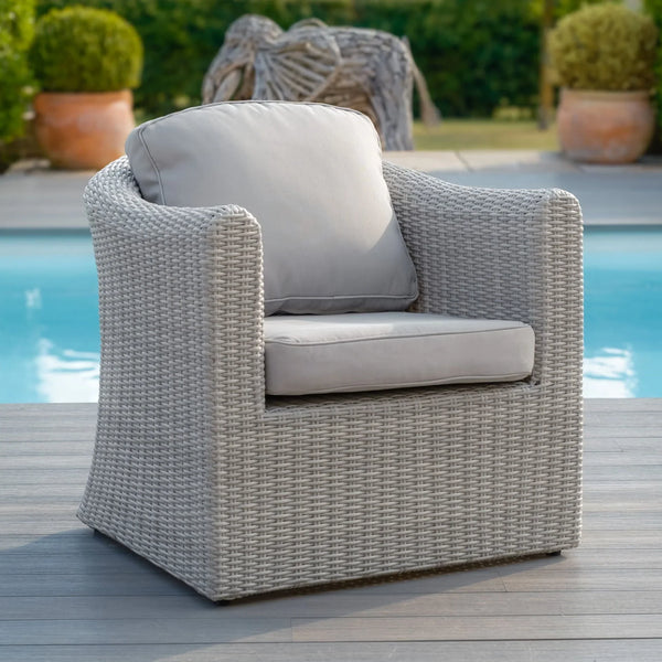Light grey rattan outdoor armchair with cushions beside pool on wood decking