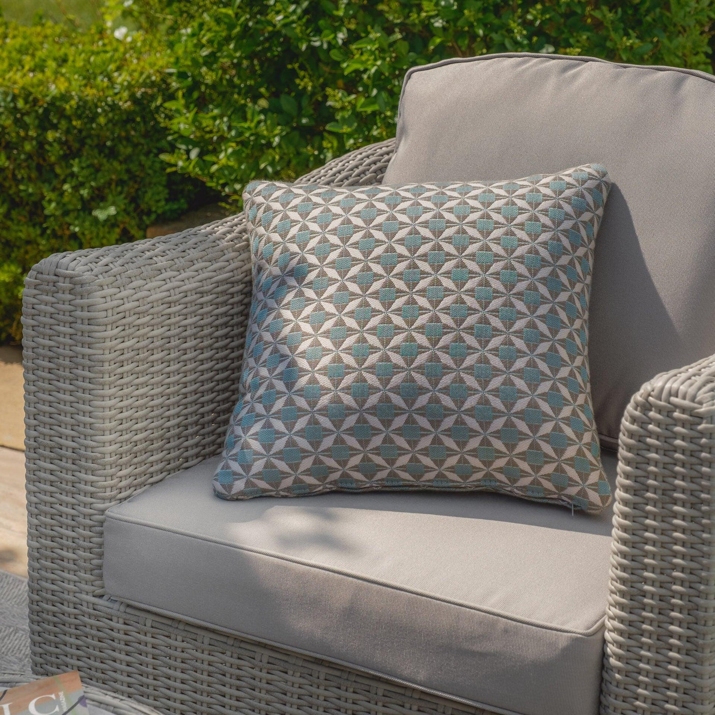 Grey rattan garden armchair with beige cushion and patterned geometric outdoor pillow