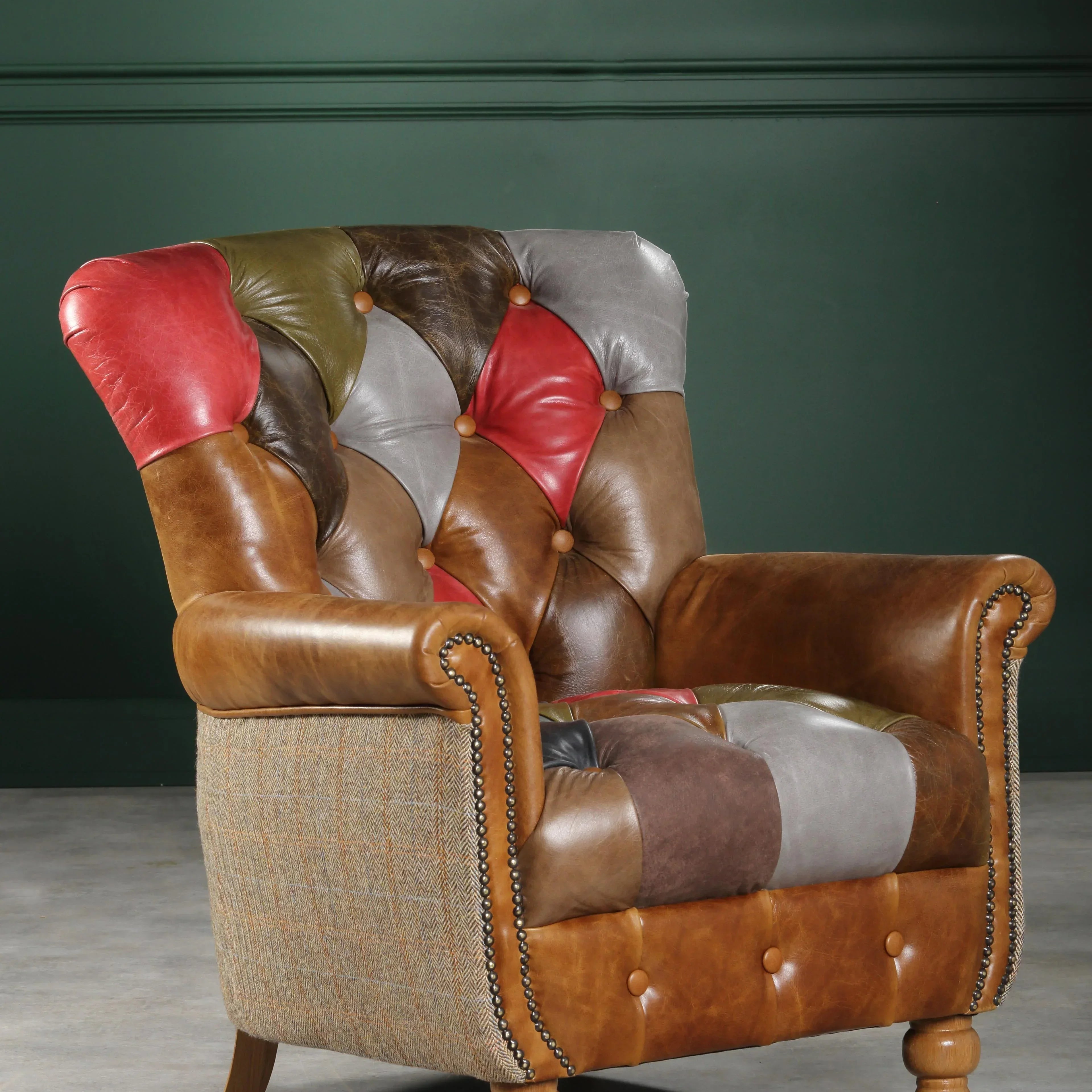 Patchwork leather armchair with studded detailing and turned wooden legs against dark green wall