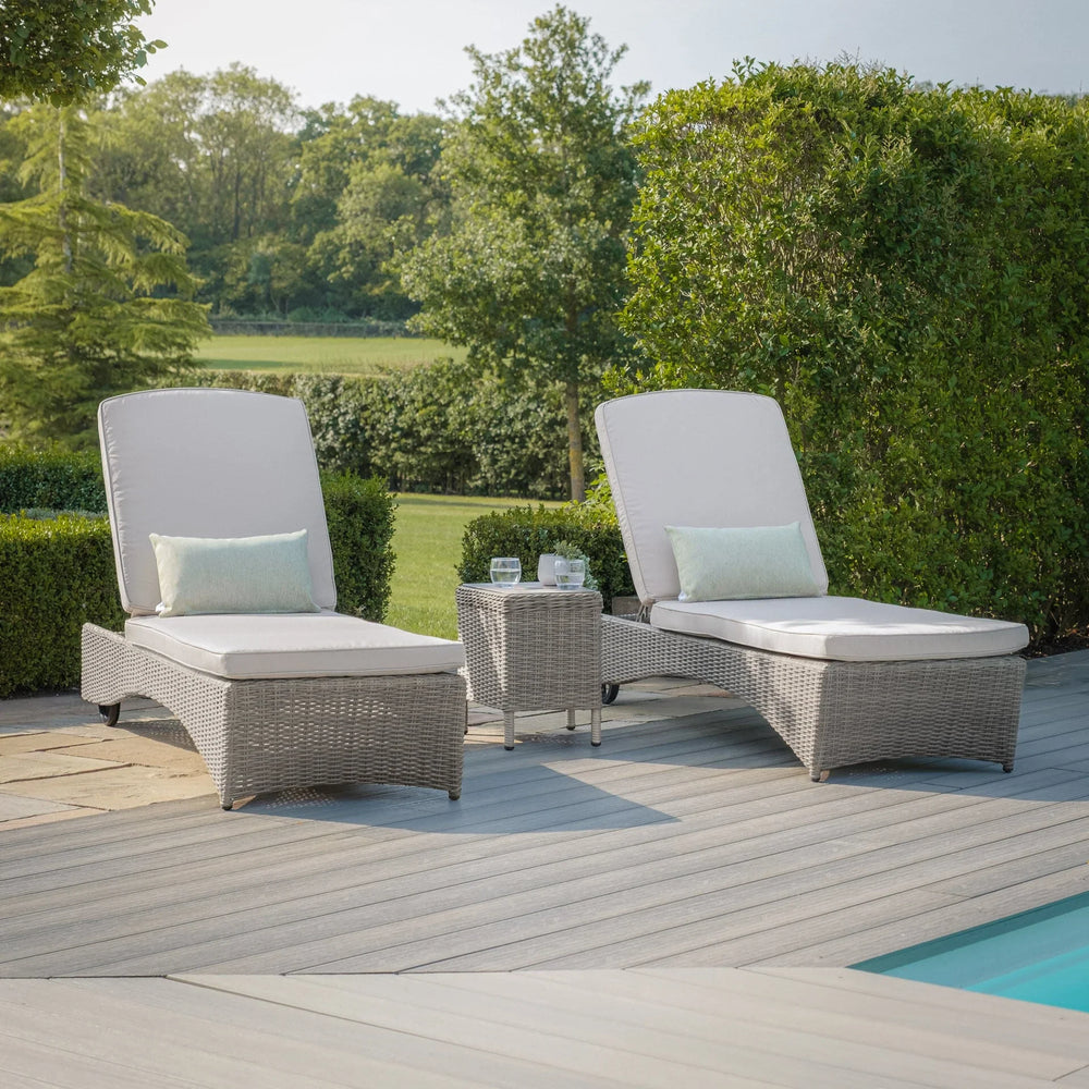 Grey rattan sun loungers with cream cushions and side table by a pool on patio