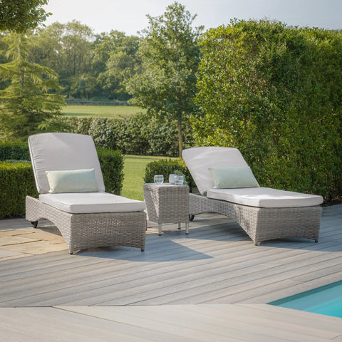 Grey rattan sun loungers with cushions and side table by pool on decking