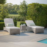 Grey rattan sun loungers with cushions and side table by pool on decking