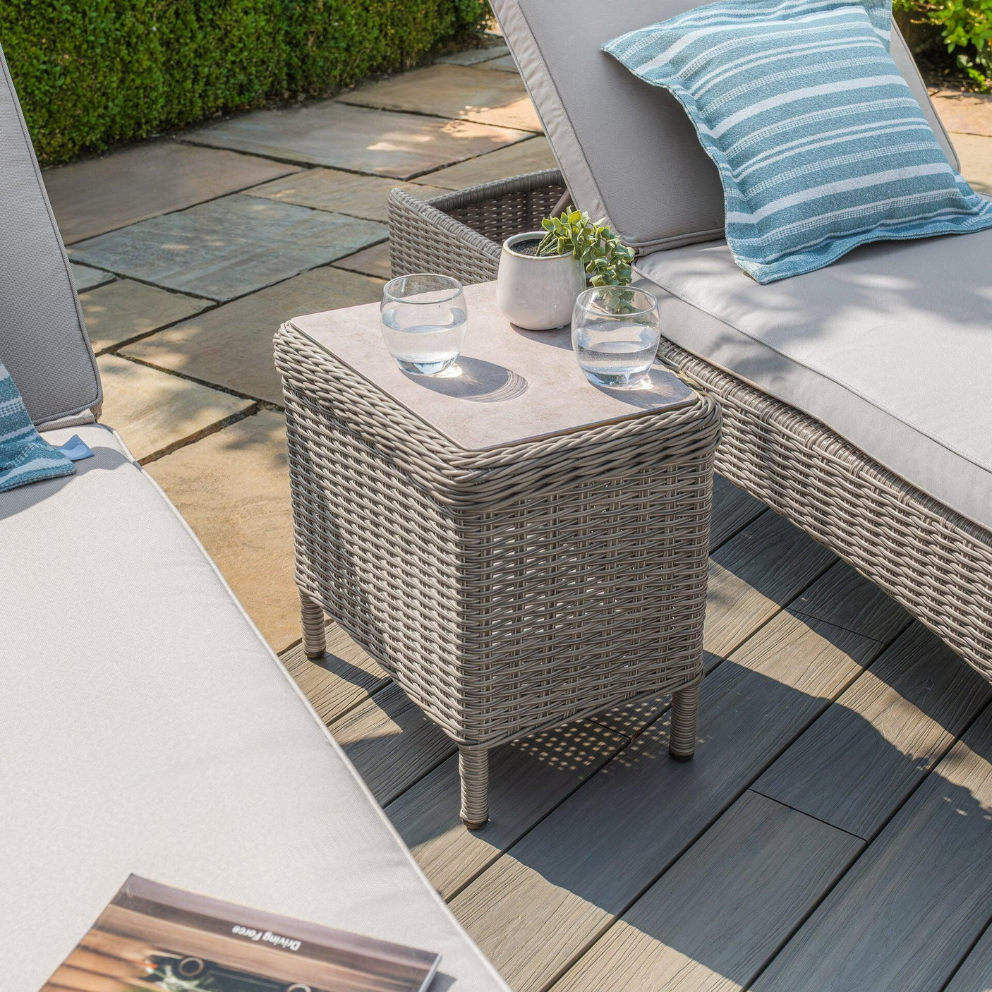 Grey rattan garden side table with glass top beside outdoor loungers on patio