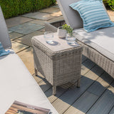 Grey rattan garden side table with glass top beside outdoor loungers on patio