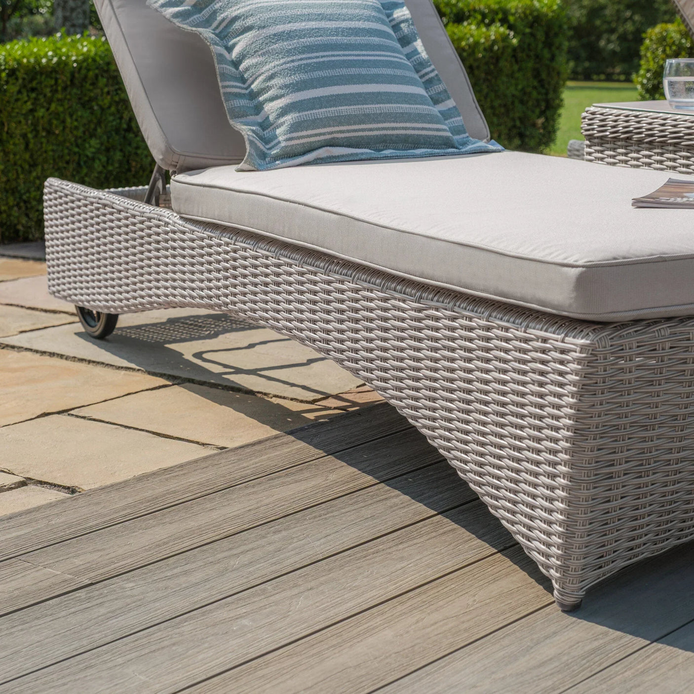 Grey rattan sun lounger with cushion and striped pillow on patio decking