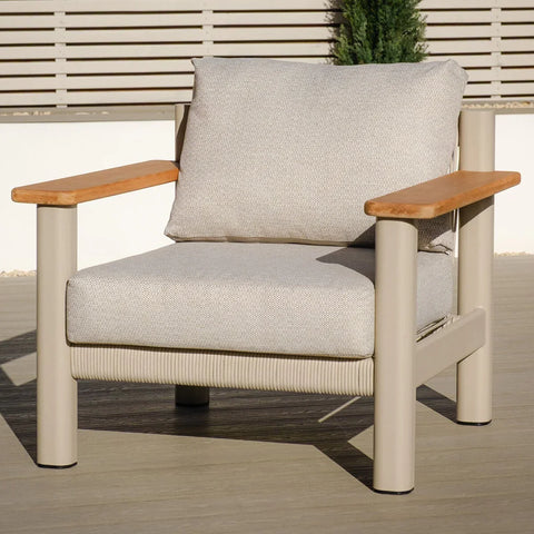 Beige outdoor armchair with light wood armrests and thick cushions on patio
