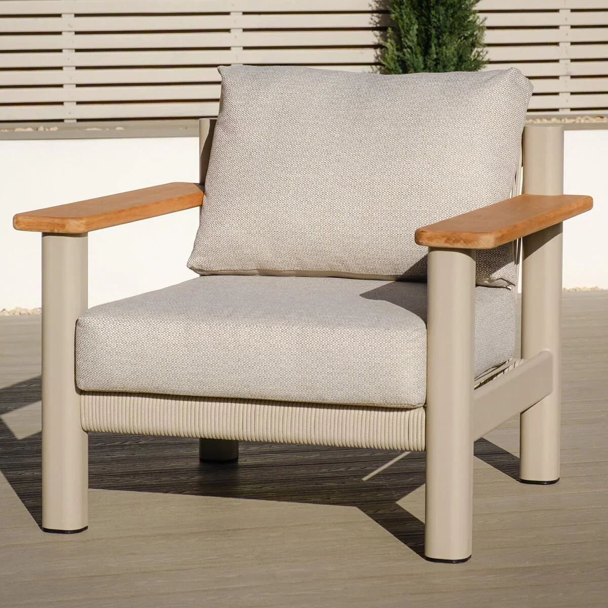 Beige outdoor armchair with light wood armrests and thick cushions on patio