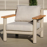 Beige outdoor armchair with light wood armrests and thick cushions on patio