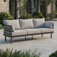 Outdoor patio sofa with light grey cushions and dark metal frame on stone flooring